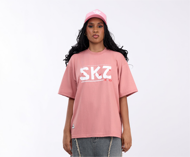 Person wearing a pink 'SKZ' t-shirt and cap on a white background